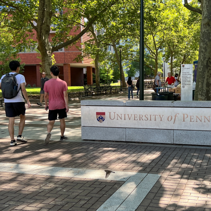 Two students walking onto campus passing a sign that reads "University of Pennsylvania"