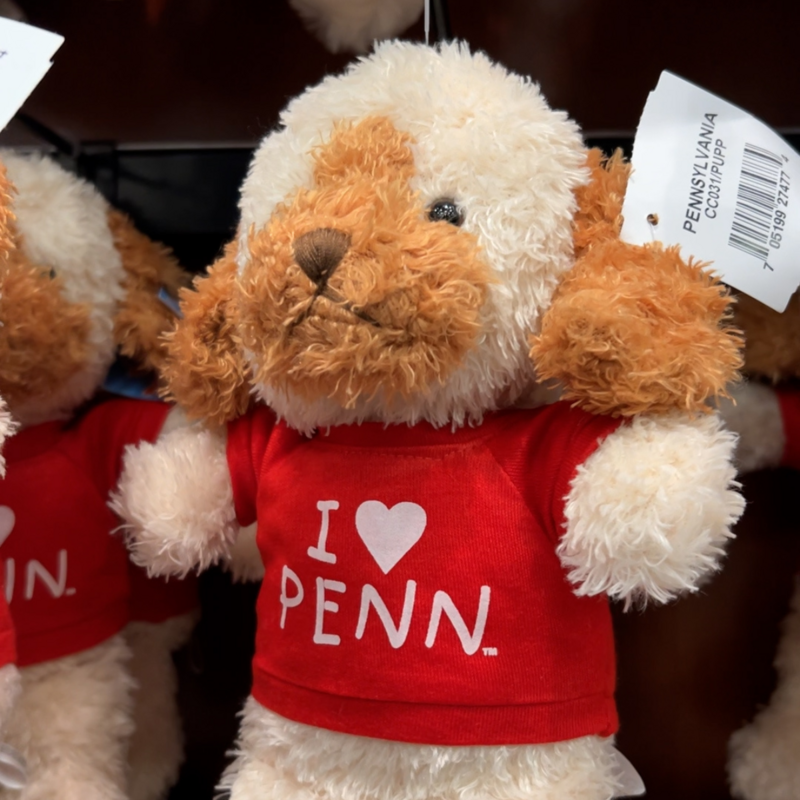 White and brown dog stuffed animal wearing a red shirt that reads "I heart Penn"