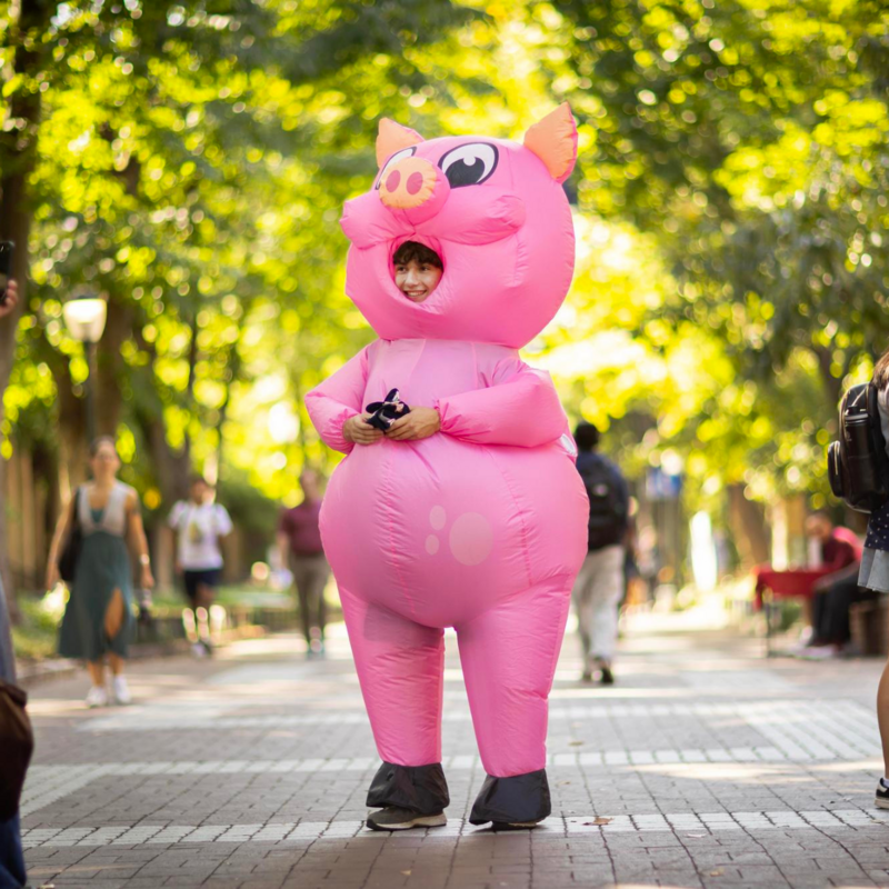 Student standing on Locust Walk dressed as Financial Wellness mascot Penny the Pig 