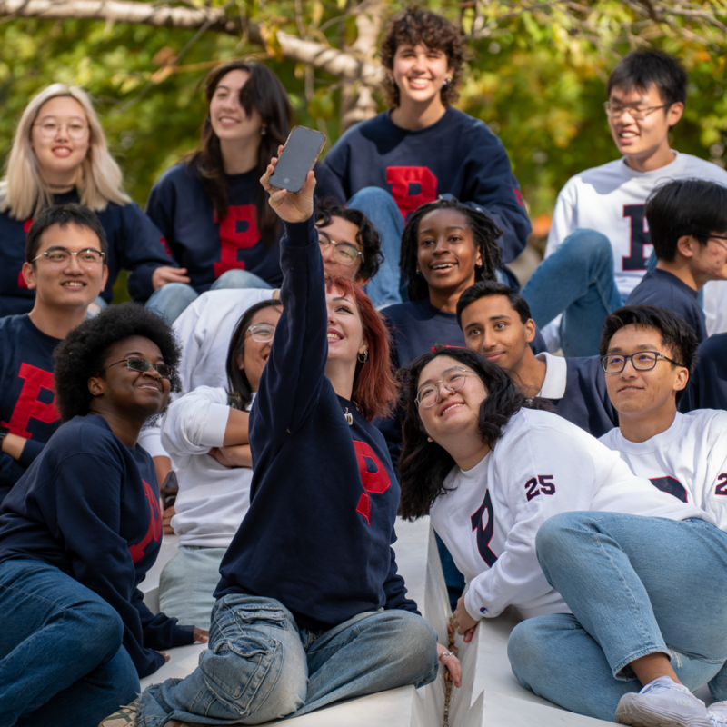 Large group of Penn students taking a selfie while sitting on the button wearing matching Penn sweatshirts.